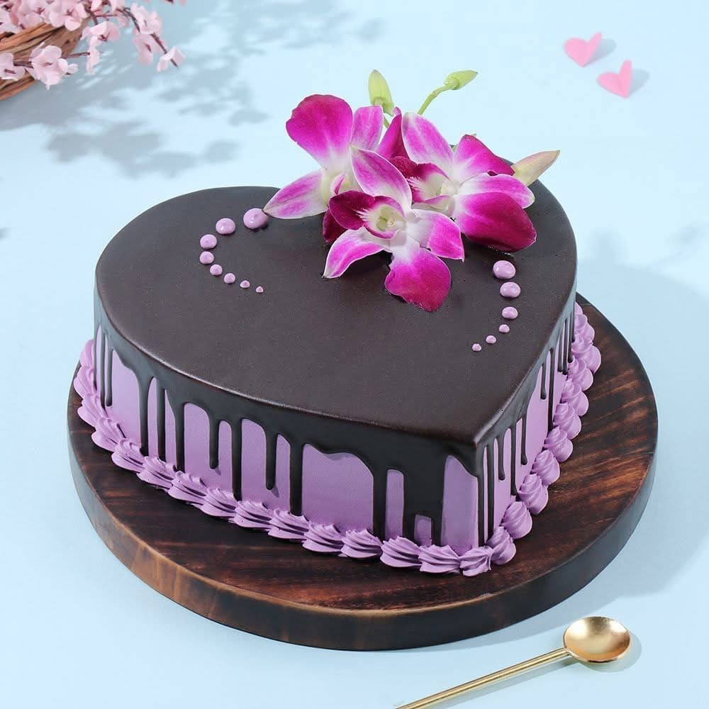 Heart-shaped chocolate cake with purple icing and orchid flowers on a wooden board.