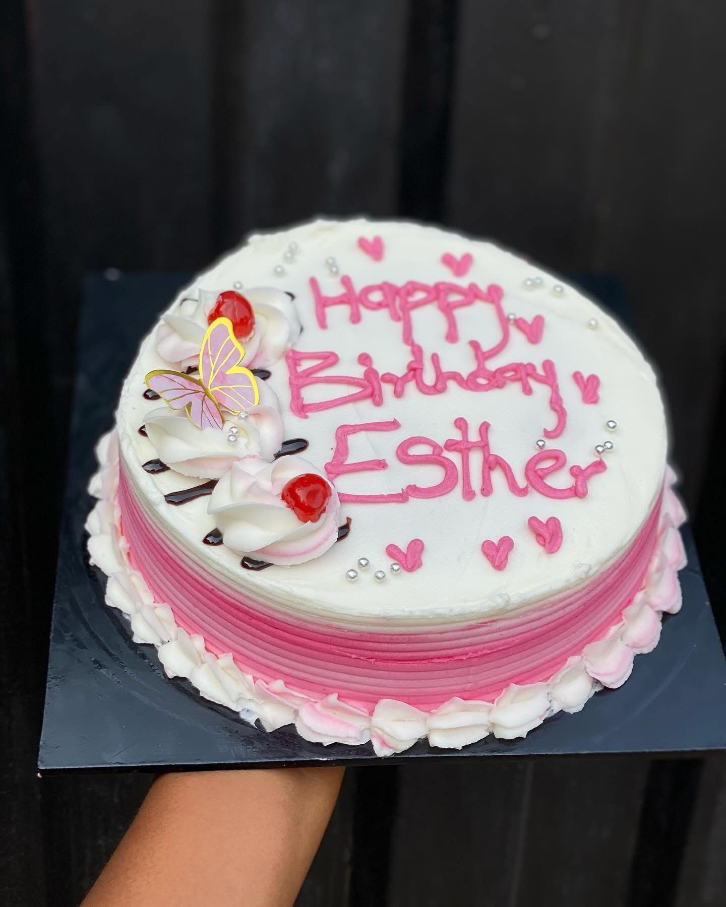 Round pink and white birthday cake with piped text and floral decorations.
