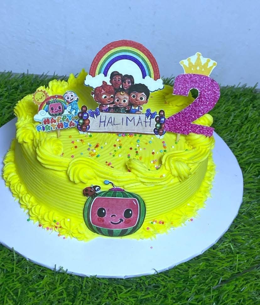 Yellow birthday cake with cartoon decorations, a rainbow, and the number 2.