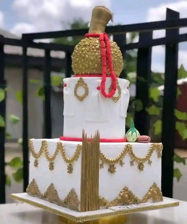 Elegant tiered cake with gold and red decorations resembling traditional attire, displayed outdoors.