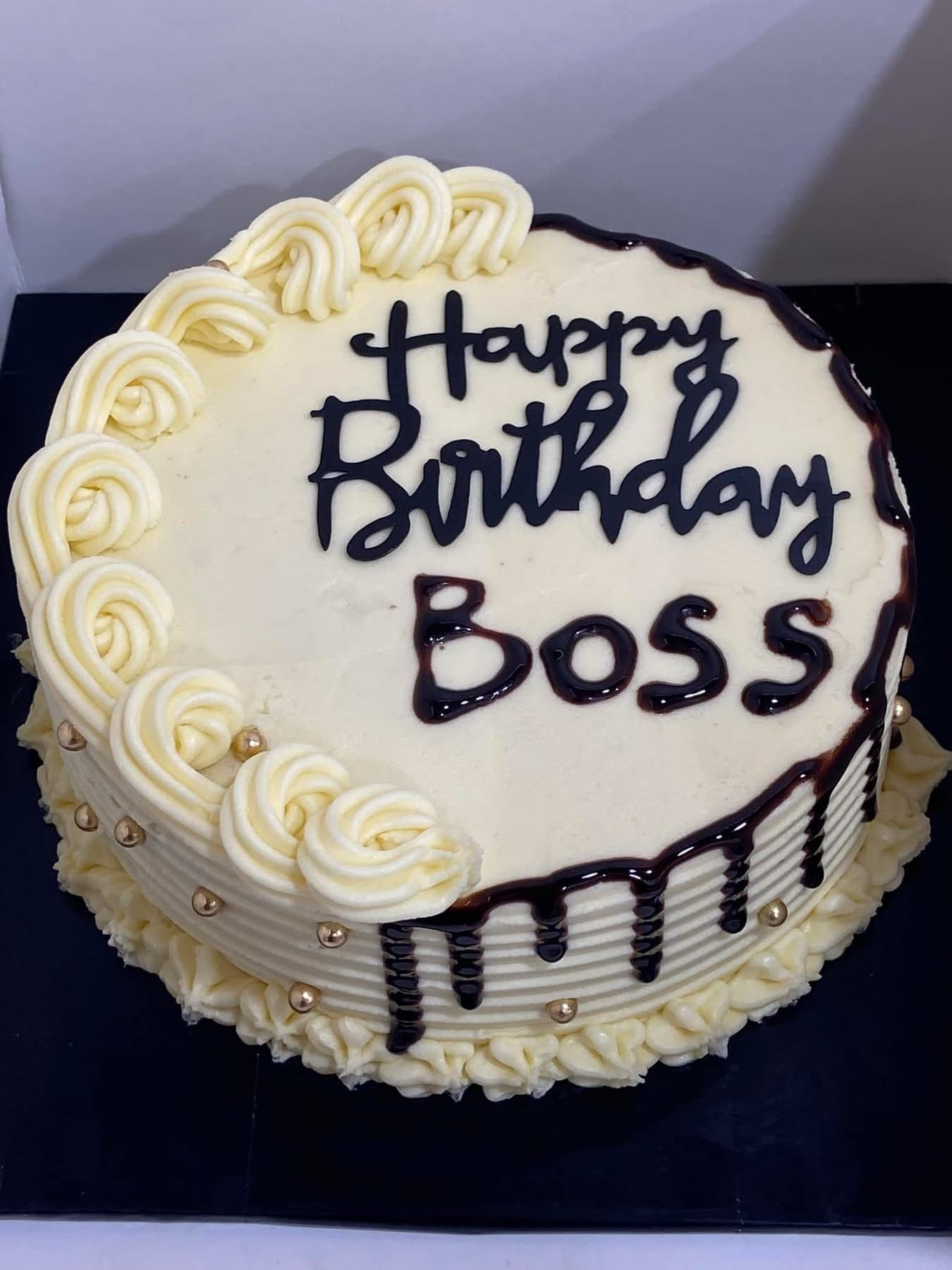 Vanilla birthday cake with 'Happy Birthday Boss' written on top and chocolate drizzle.