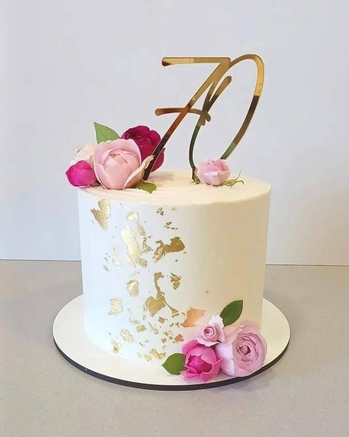 White cake with golden accents, topped with pink roses and a gold number 70 decoration.