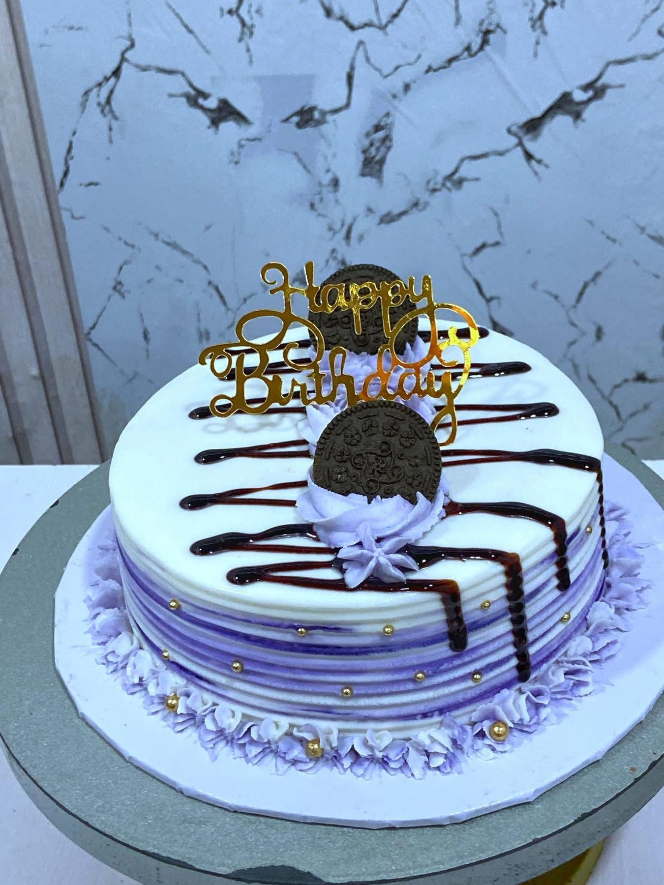 Birthday cake with chocolate drizzle, purple accents, and a 'Happy Birthday' topper.