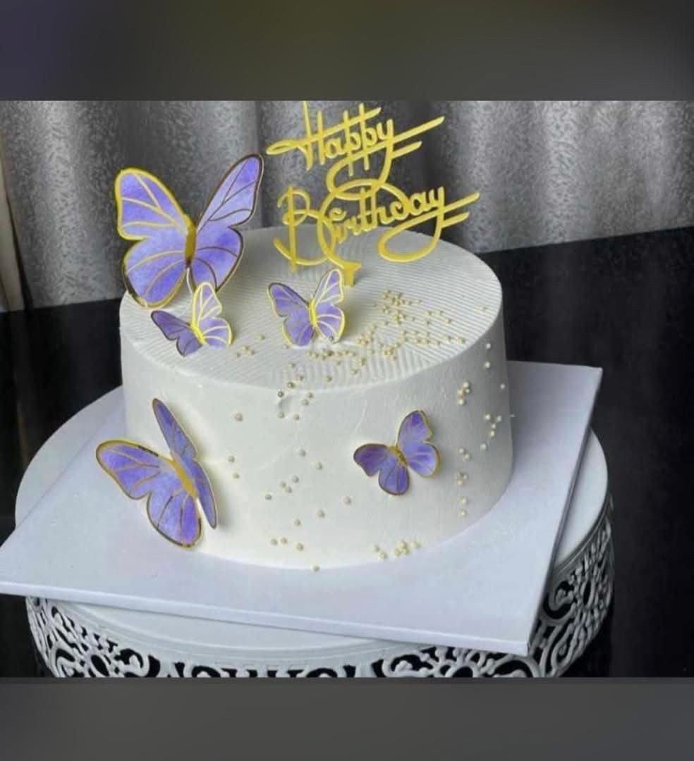 White birthday cake with purple butterfly decorations and 'Happy Birthday' topper.