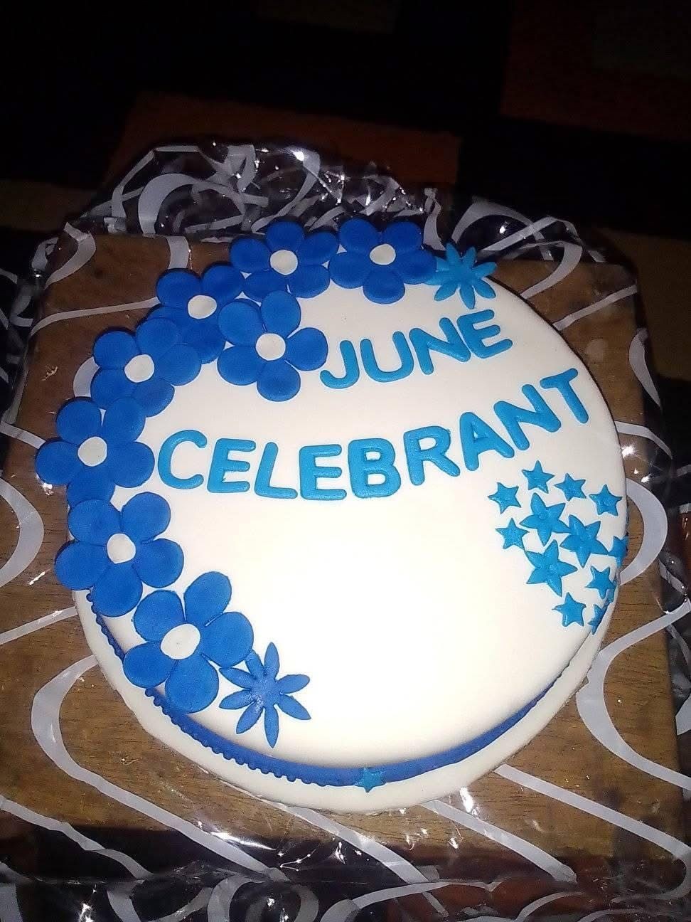 Round white cake with blue floral decorations and text 'June Celebrant' written in blue icing.