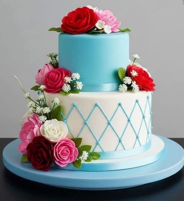 Two-tier blue and white cake decorated with red, pink, and white flowers and green leaves.