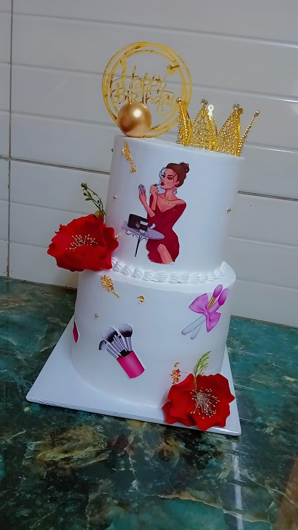 Two-tier cake with gold crown, red flowers, and makeup-themed decorations.