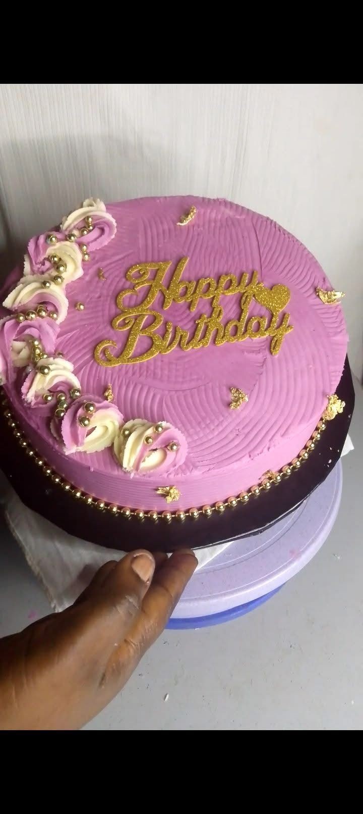 Pink birthday cake with gold decorations and piped flowers.