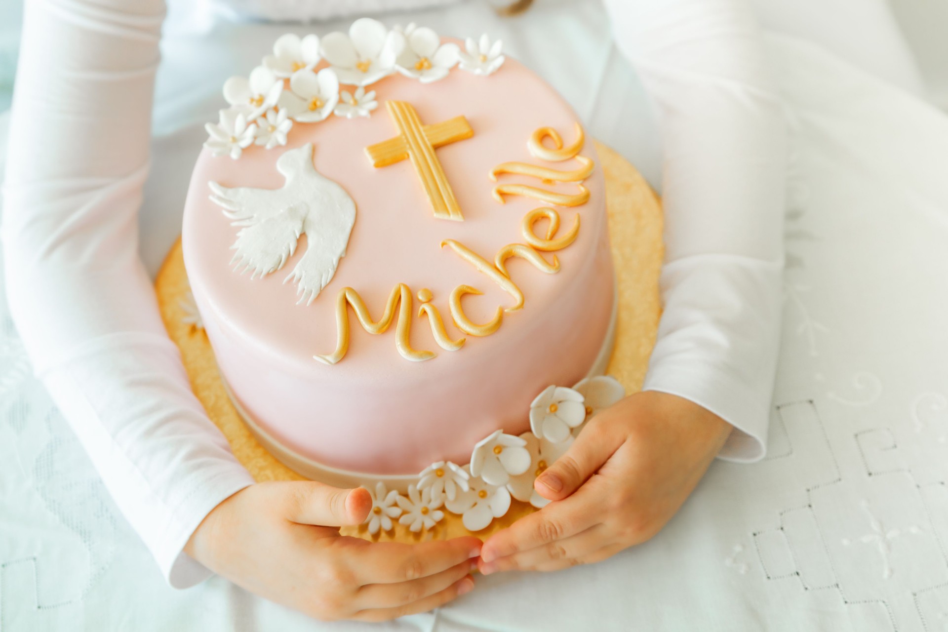 In the hands of a girl there is a birthday cake, a first communion cake, a baptism cake with beautiful flowers, a dove and a cross, traditions in the Christian faith, religion, religious. Pastry