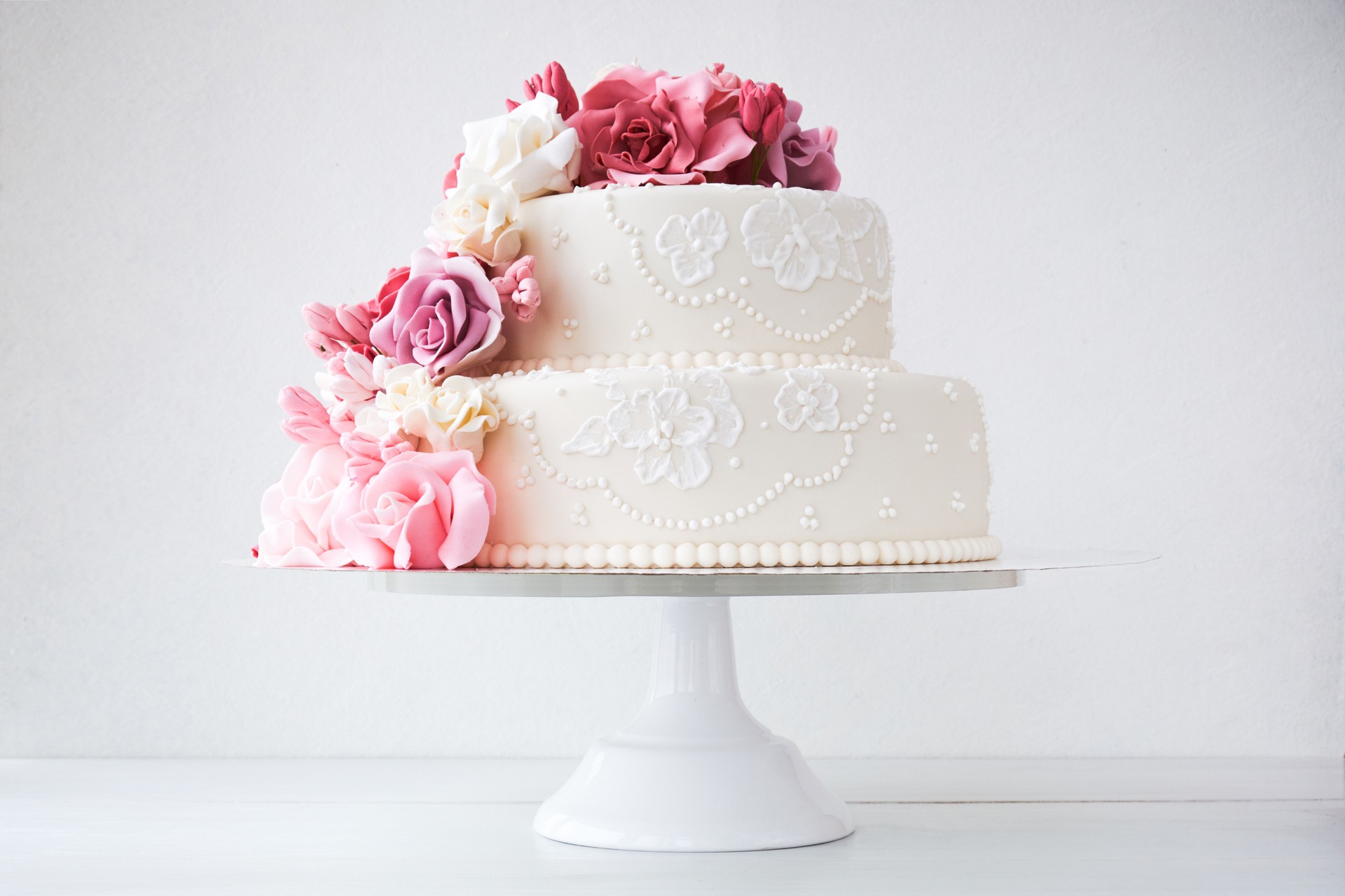 Two-tiered white wedding cake decorated with pink flowers