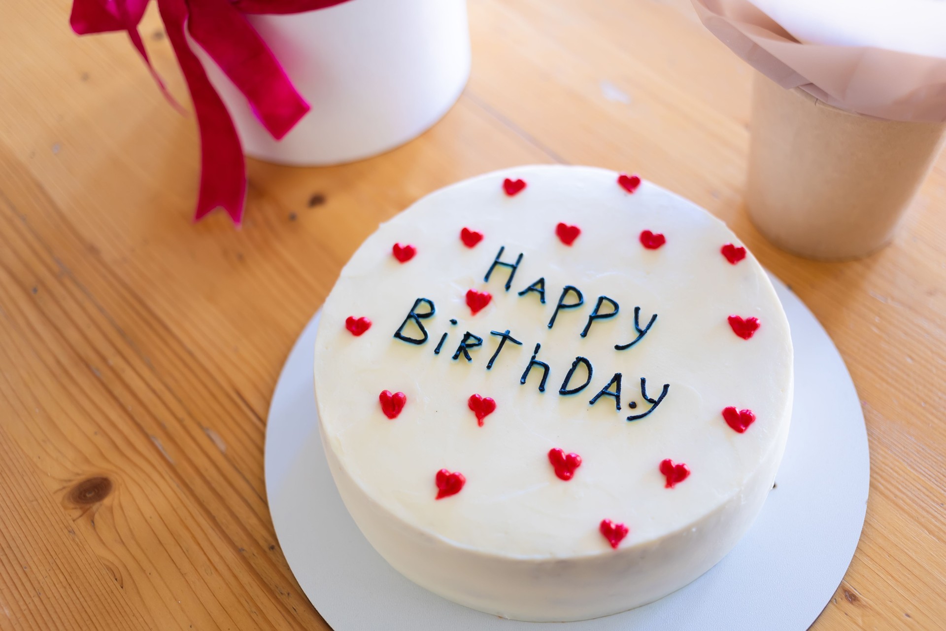 Birthday cake with the words Happy Birthday written on it, surrounded by red heart decorations.