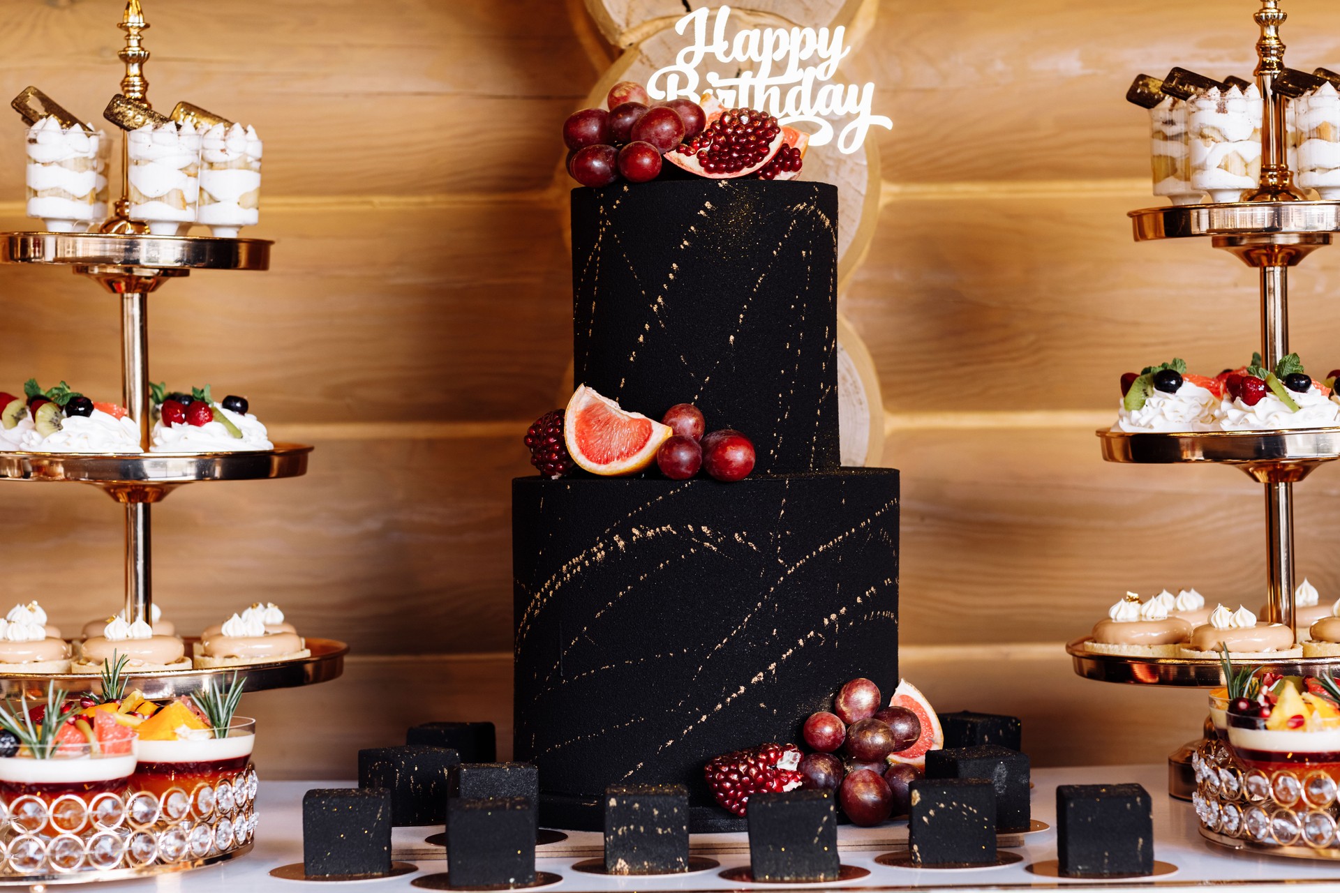 big black birthday cake with fresh fruits and sweets on a festive table. Candy bar. Table with different sweets for party