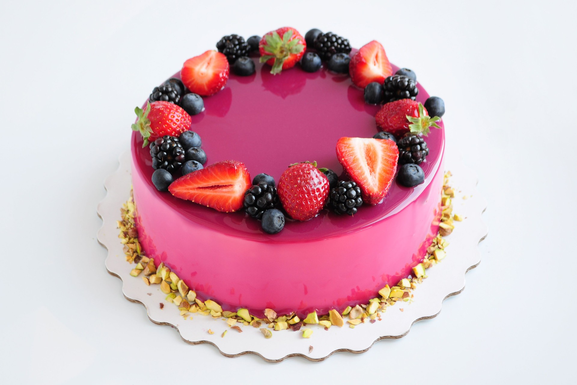 Mousse cake with pink mirror glaze, berries, pistachios.