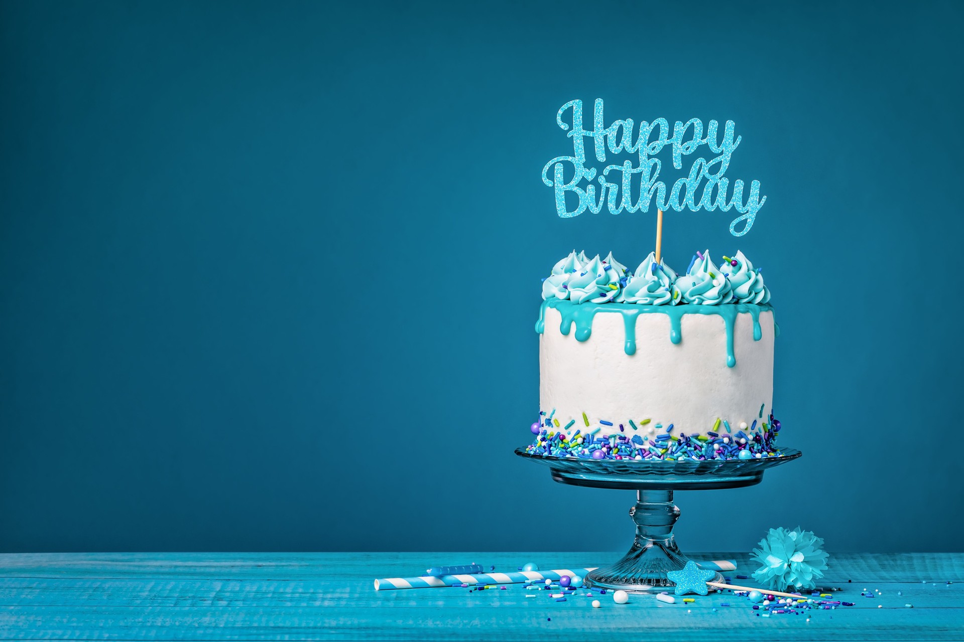 White happy birthday cake with teal ganache over a blue background