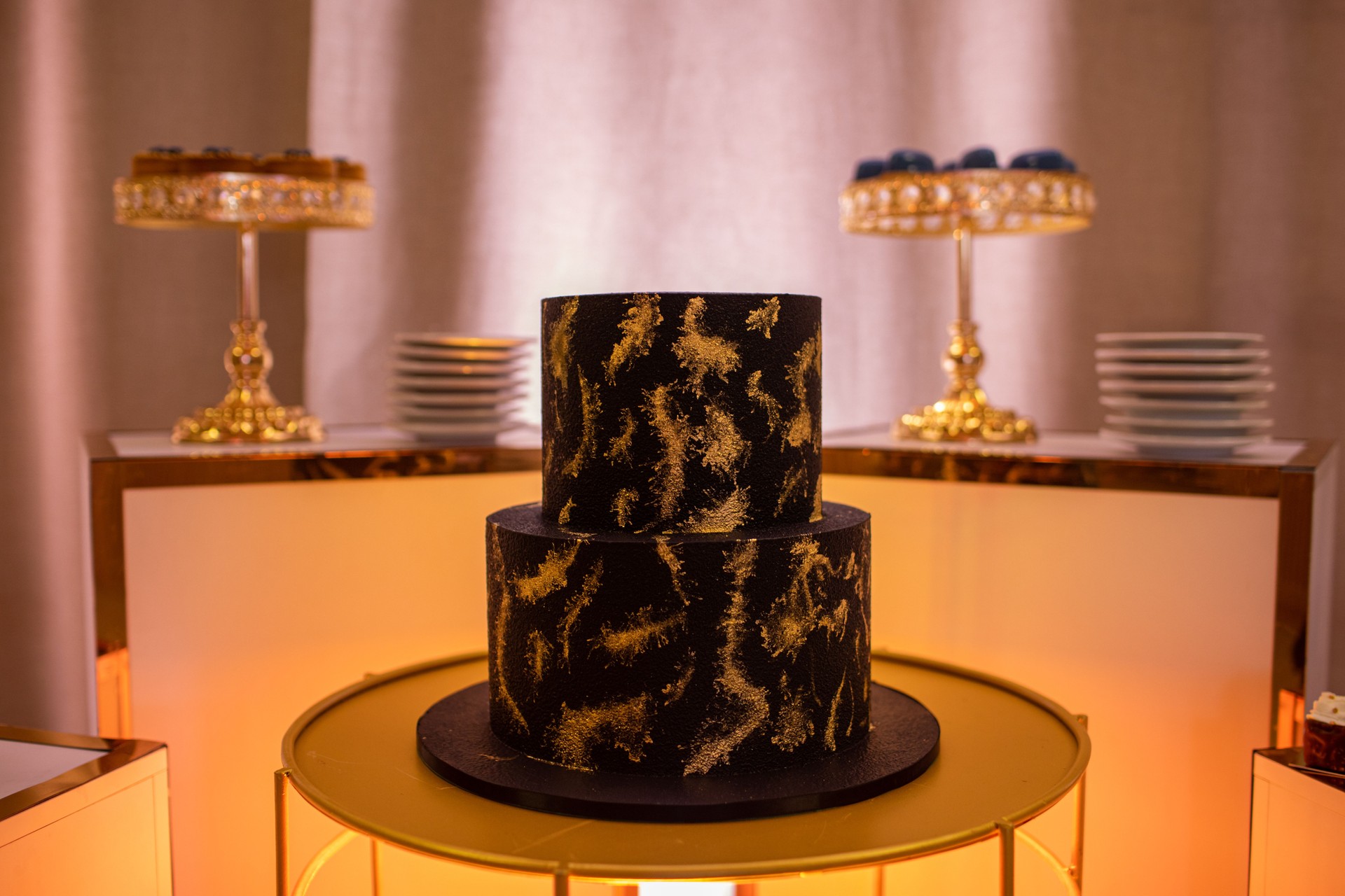 Luxury candy bar. Festive chocolate two-tiered cake decorated golden decor on table for party, birthday, valentines day, wedding. Assortment of delicious dessert and plates on stands on background