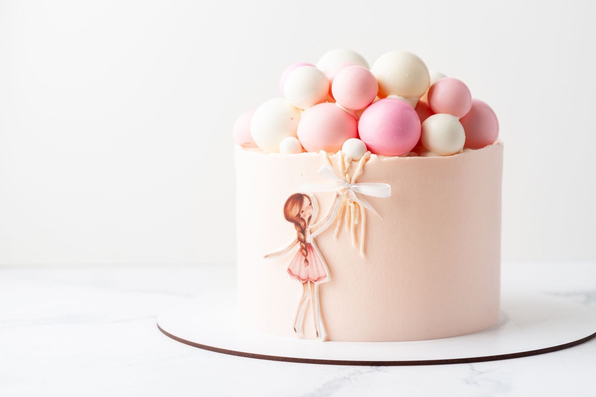 Birthday cake for a girl with chocolate spheres decoration on top. Little girl holding air balloons.